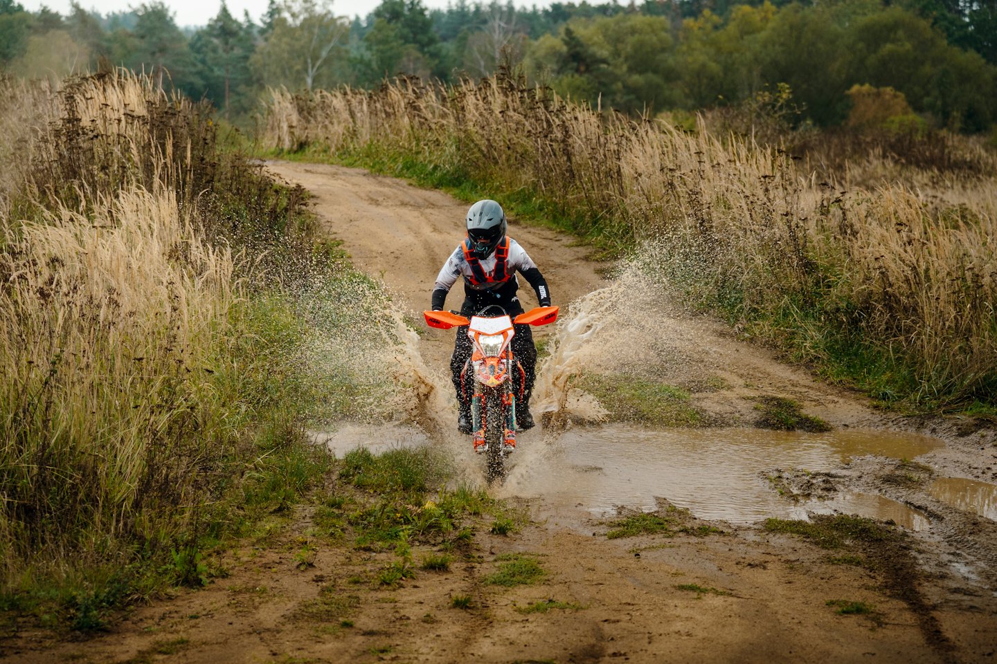 Motocyklista crossowy chlapiący przez błotnistą kałużę na torze.